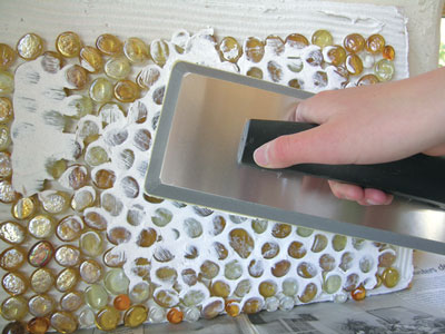 5. Using a rubber tile float, squeeze a layer of white tile grout into the crevices around the glass globs.